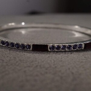 May include: A silver bangle bracelet with a row of purple and red rhinestones.