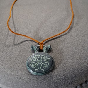 May include: A brown leather cord necklace with a round, green and black pendant featuring a geometric design.