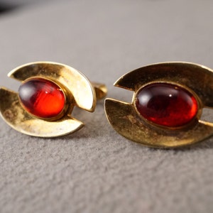 May include: A pair of gold cufflinks with red oval-shaped glass stones set in the center.