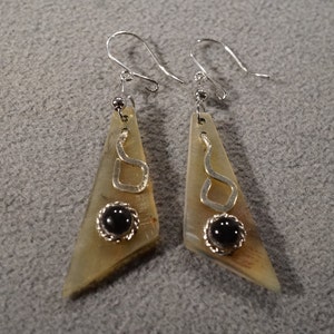 May include: A pair of dangle earrings with a triangular shaped horn pendant. Each pendant has a silver swirl design and a black stone in the center.