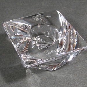 May include: Clear crystal candle holder with a square shape and a circular indentation for a candle. The word "Darling" is etched on the side. The Orrefors logo is visible.
