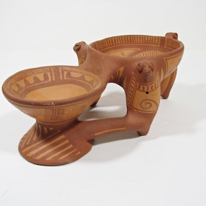 Puede incluir: Un plato de servir de cerámica de terracota con tres cuencos. El plato está decorado con patrones geométricos y tiene tres patas con forma de animal.