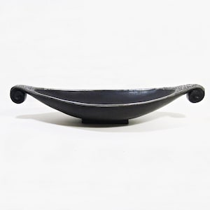 Könnte beinhalten: Eine schwarze dekorative Schale mit silbernem Rand und gerollten Enden. Die Schale hat eine bootsartige Form und steht auf einem kleinen rechteckigen Sockel. Die Enden der Schale haben ein strukturiertes Design.