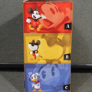 May include: A colorful box featuring three Disney character figurines: Mickey Mouse, wearing red shorts and yellow shoes; Mickey Mouse with sunglasses; and Donald Duck. The box has a red, yellow, and blue color scheme.