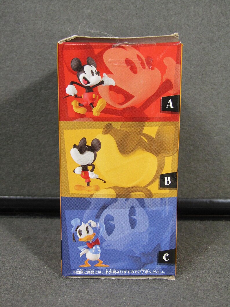 May include: A colorful box featuring three Disney character figurines: Mickey Mouse, wearing red shorts and yellow shoes; Mickey Mouse with sunglasses; and Donald Duck. The box has a red, yellow, and blue color scheme.