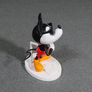 May include: A figurine of Mickey Mouse wearing sunglasses, red shorts, yellow shoes, and white gloves. The black and white figure is posed on a white base with a white support. The figurine is a collectible item.