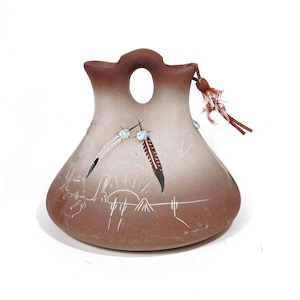 May include: A handcrafted, brown ceramic vase with a unique shape and a decorative feather design. The vase features a central opening and is adorned with etched lines and a small tassel. The color palette includes shades of brown and white.