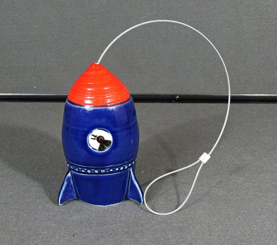A ceramic rocket ship that doubles as a hanging air plant holder — retro space-age aesthetic meets functional living-plant display, handmade in the USA.