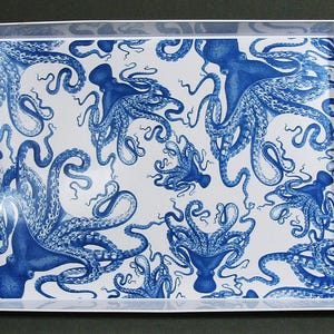May include: Rectangular serving tray with a white background and a repeating pattern of blue octopuses. The tray has a white border with integrated handles, offering a nautical or coastal theme. The octopus illustrations are detailed and artistic.