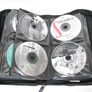 May include: Black CD carrying case filled with various music CDs. The CDs are in clear plastic sleeves. Some CD titles visible include Toby Keith's "Unleashed" and "Super Hits" by Shenandoah.