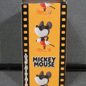 May include: A rectangular box with a yellow background featuring a cartoon image of Mickey Mouse. The box has a film strip design on the sides and the words "MICKEY MOUSE" in bold white letters.