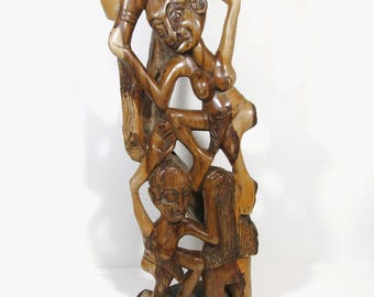 May include: A wooden sculpture featuring carved figures in a vertical composition. The figures are rendered in natural wood tones, showcasing the wood grain. The sculpture seems to represent human forms, with detailed facial features and body postures.