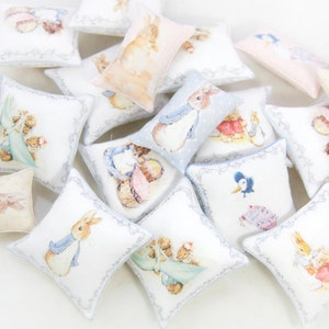 Op de afbeelding: Een verzameling kleine, vierkante en rechthoekige sierkussens met illustraties van Peter Konijn en andere personages uit de verhalen van Beatrix Potter. De kussens hebben een witte achtergrond met decoratieve randen en pastelkleurige afbeeldingen.