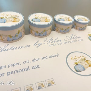 May include: Four round blue and white gift boxes with a pumpkin design and the word "Autumn" in gold lettering. The boxes are on a white surface with the text "Autumn by Pilar Alin only for personal use" and "250grs paper, cut, glue and enjoy!" in black cursive writing.