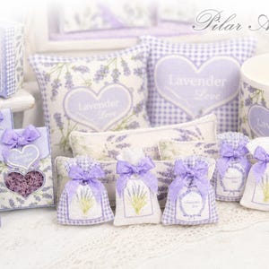 May include: A collection of lavender-themed items including small fabric sachets with purple bows, square pillows with heart motifs, and boxes featuring the text Lavender Love. The items display lavender sprig patterns and gingham accents.