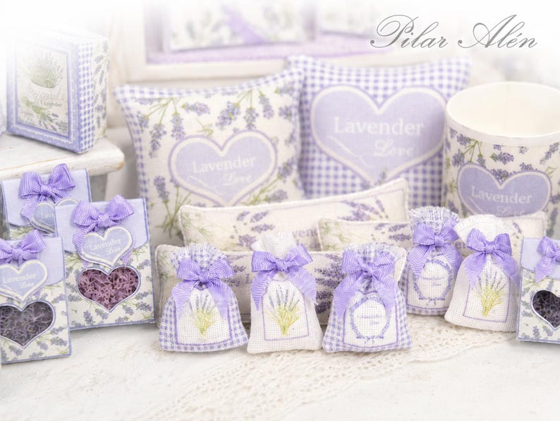 May include: A collection of lavender-themed items including small fabric sachets with purple bows, square pillows with heart motifs, and boxes featuring the text Lavender Love. The items display lavender sprig patterns and gingham accents.