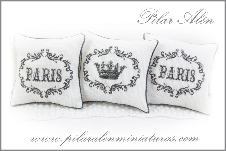 May include: Three white decorative pillows with black embroidery. The pillows feature a crown design and the word "PARIS" in a decorative font.