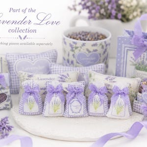 May include: A collection of lavender-themed items including small fabric sachets with purple bows, heart-shaped tags, a patterned mug, and a gift bag. The items feature lavender sprig illustrations and the text Part of the Lavender Love collection.