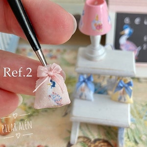 K&ouml;nnte beinhalten: Eine rosa Stofftasche mit einem blauen und wei&szlig;en Vogelmuster und einem rosa Band. Die Tasche wird in einer Hand gehalten, wobei der Text "Ref.2" sichtbar ist. Die Tasche ist ein Miniaturartikel.