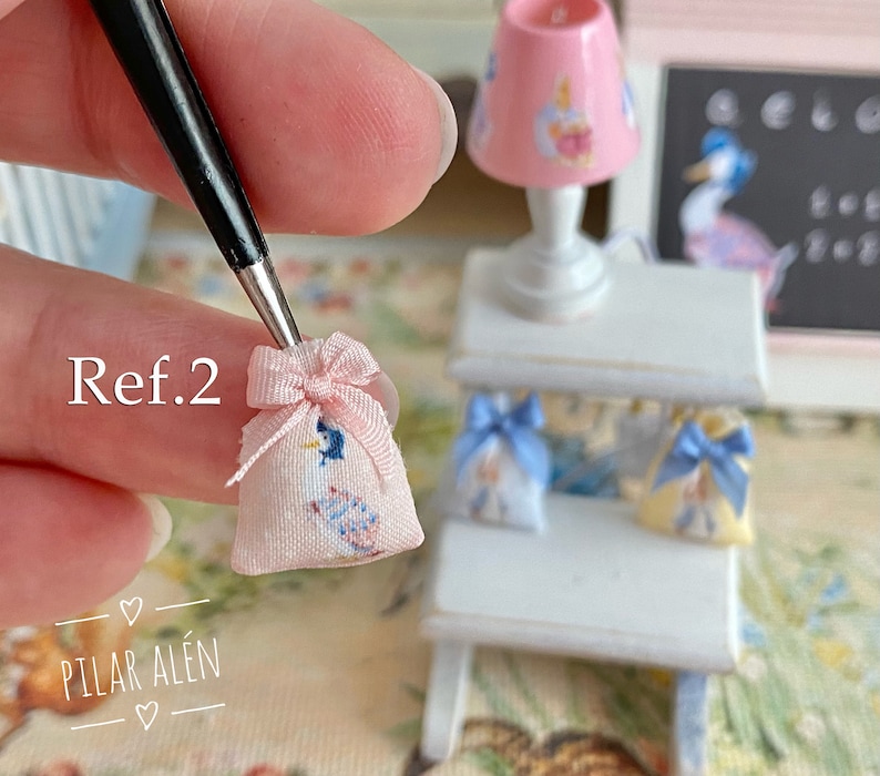 K&ouml;nnte beinhalten: Eine rosa Stofftasche mit einem blauen und wei&szlig;en Vogelmuster und einem rosa Band. Die Tasche wird in einer Hand gehalten, wobei der Text "Ref.2" sichtbar ist. Die Tasche ist ein Miniaturartikel.