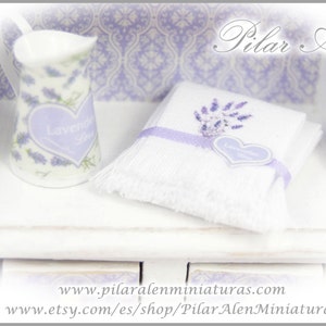 May include: White ceramic pitcher with a lavender design and the words "Lavender Joy" on the front. The pitcher is sitting on a white shelf with a white towel with a lavender design and a heart-shaped tag that says "Lavender Joy".