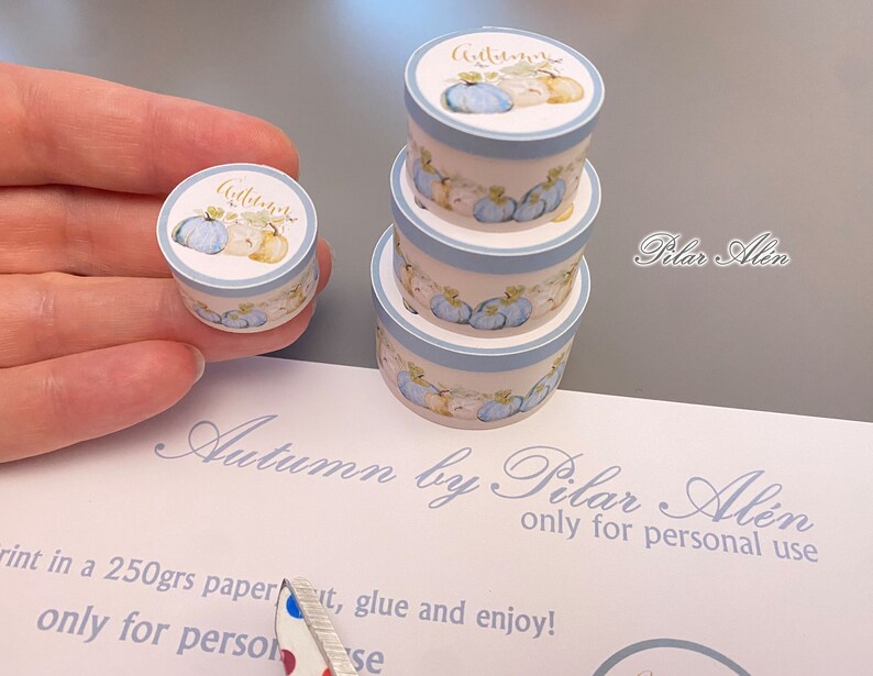 May include: A set of three blue and white paper boxes with a watercolor design of pumpkins and the word "Autumn" in gold lettering. The boxes are stacked on top of each other and are being held in a hand. The boxes are for personal use only.