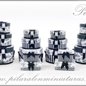 Könnte beinhalten: Ein Satz schwarzer und weißer Geschenkboxen mit schwarzen Schleifen. Die Boxen sind in verschiedenen Größen gestapelt und in einer Reihe angeordnet. Die Boxen sind mit einem schwarzen und weißen Muster aus Blumen und Blättern verziert. Die Boxen sind mit dem Text "Pilar Alen" beschriftet.