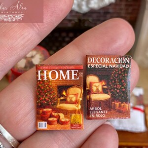 May include: Miniature Christmas magazines with detailed covers. One features a fireplace and the word "HOME", the other says "DECORACION ESPECIAL NAVIDAD". Both are held in a hand, showcasing their small size.