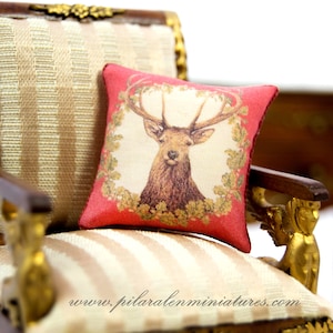 Può includere: Una poltrona in miniatura con rivestimento a strisce rosse e crema. La poltrona ha una struttura dorata e un cuscino decorativo con un motivo di cervo. Il cuscino ha uno sfondo rosso con un cervo color crema e fogliame dorato.