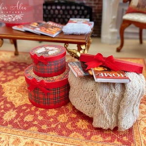 May include: Miniature Christmas-themed decor featuring two plaid gift boxes with red bows, a small table with magazines, and a decorative knitted pouf with more magazines and a red ribbon. The scene is set on a patterned rug.