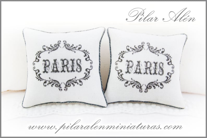 May include: Two white decorative pillows with black embroidery that reads "PARIS" in a decorative font. The pillows are on a white surface.