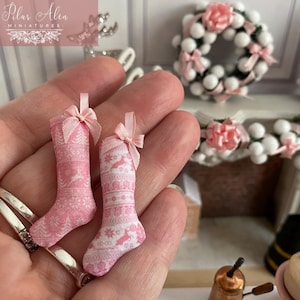 Può includere: Due calze di Natale rosa e bianche con un motivo a fiocco di neve. Le calze sono tenute in una mano.