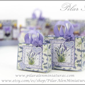 May include: Two miniature paper shopping bags featuring a lavender floral pattern on a cream background. Each bag has light purple ribbon handles, a small heart-shaped tag labeled Lavender Love, and a decorative bow. The text Pilar Alén is visible.