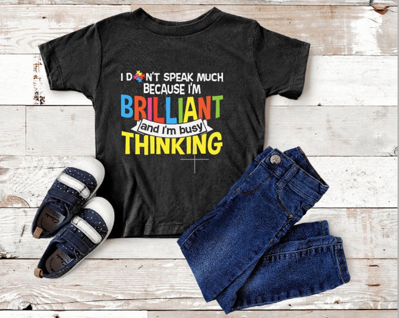 May include: Black toddler t-shirt with the text "I don't speak much because I'm brilliant and I'm busy thinking." The shirt is paired with blue jeans and navy blue and white sneakers.