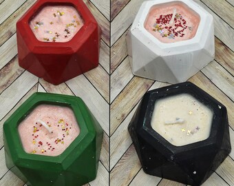 Puede incluir: Cuatro portavelas de hormigón geométricos con velas rosas, blancas y beige. Cada portavelas tiene un color diferente: rojo, blanco, verde y negro.