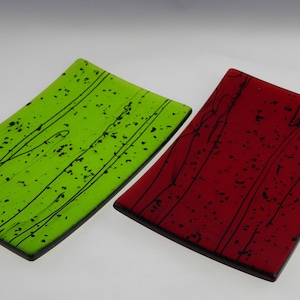 Puede incluir: Dos platos de servir rectangulares de vidrio con líneas negras y motas. Un plato es verde y el otro es rojo.