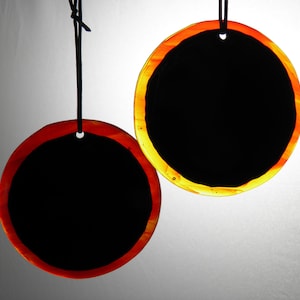May include: Two round black glass ornaments with a red and orange rim. The ornaments are hanging from black cords.