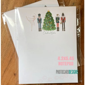 May include: A notepad with a Christmas theme, featuring a ballerina, nutcrackers, and a decorated Christmas tree. The notepad measures 4.2 x 5.45 inches and has the text "Christmas Wishes". The brand name "PHOTOCARDDESIGNS" is also visible.