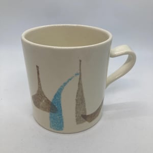 May include: Cream-colored ceramic mug with a curved handle. The mug features a simple design of brown and blue abstract shapes. The mug is suitable for coffee, tea, or other beverages.