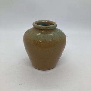 May include: A small, handcrafted ceramic vase with a rounded body and a slightly flared rim. The vase features a speckled, earthy brown base that transitions to a muted green at the top. The interior of the rim has a hint of blue.