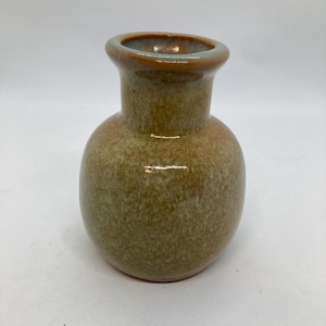 May include: A small, round ceramic vase with a narrow neck and a wide opening. The vase has a speckled, earthy green and brown glaze. The rim is a darker brown with a hint of green. The vase is suitable for displaying small flowers or as a decorative item.