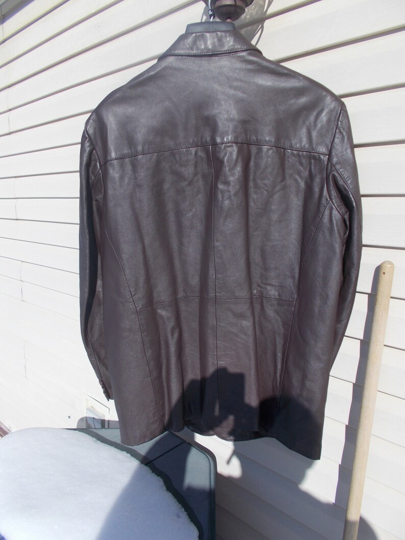 May include: A brown leather jacket with a button-up collar and long sleeves.