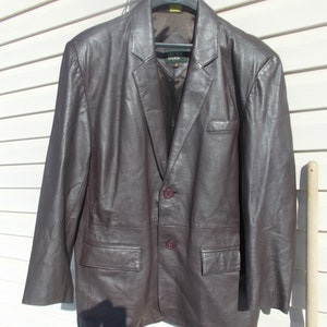 May include: A brown leather blazer with a two-button closure and two front pockets. The blazer has a label that reads "Irvine Park".
