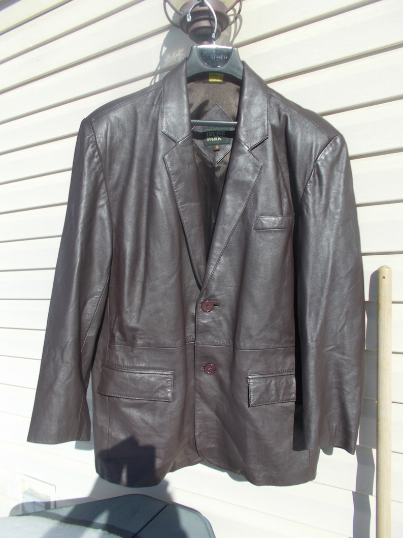 May include: A brown leather blazer with a two-button closure and two front pockets. The blazer has a label that reads "Irvine Park".