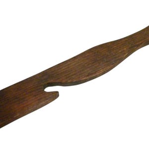 May include: A wooden butter spreader with a dark brown finish. The spreader has a long handle and a forked end, ideal for spreading butter or other soft foods. The wood grain is visible.