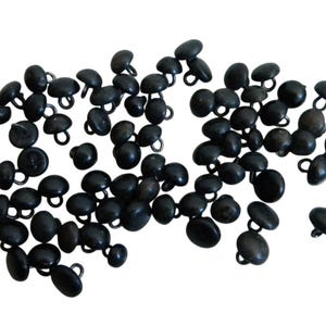 May include: A collection of small, dark gray buttons with a rounded, domed shape and a metal loop on the back for sewing. The buttons are scattered across a white background, suggesting a craft or sewing project.
