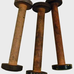 May include: Three antique wooden spools with a dark, aged appearance. Each spool has a cylindrical body and a circular, flat top and bottom. The wood shows signs of wear and age, with variations in color and texture.