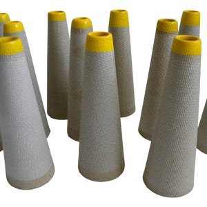 May include: A collection of ten empty textile cones arranged in a group. Each cone features a textured, light gray paper body with a distinct, bright yellow rim at the top opening. The cones are tapered in shape and stand upright on a white background.