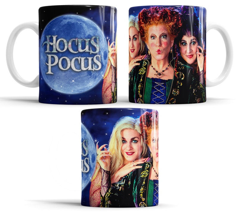 Op de afbeelding: Een witte keramische mok met drie heksen uit de film Hocus Pocus. De mok heeft een zwarte achtergrond met een blauwe maan en de woorden "Hocus Pocus" in wit.