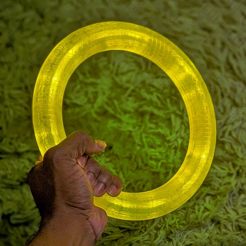 Puede incluir: Un anillo de luz amarillo brillante, sostenido en una mano, sobre un fondo verde.
